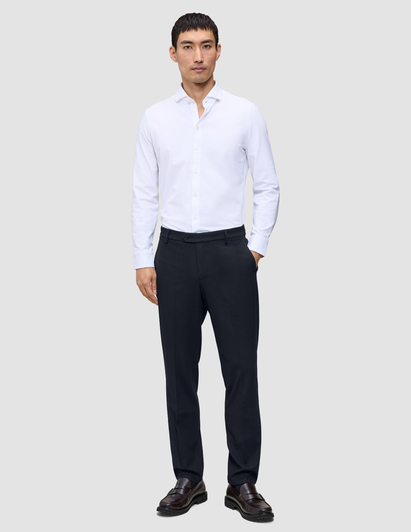 En mann kledd i en hvit skjorte, Motion Suit-bukser i regular-passform i midnattsblått og brune loafers.